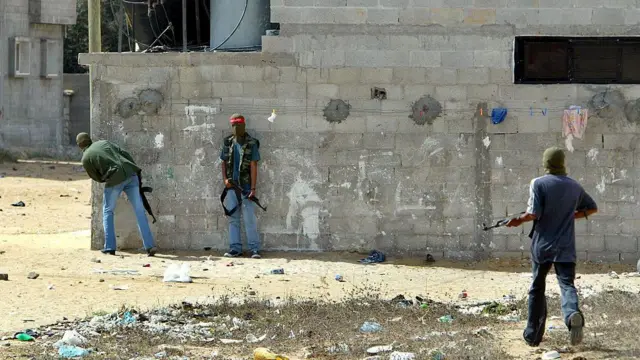 سه مرد مسلح نقاب‌پوش پشت یک دیوار