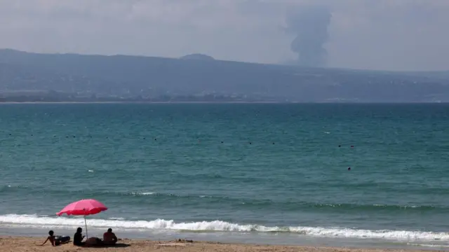 空爆でイスラエルとの国境付近で煙が上がるのを見る海水浴客たち