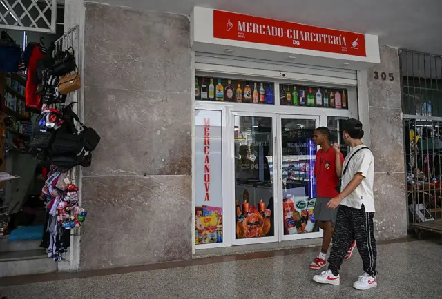 Cubanos pasan frente a comercio.