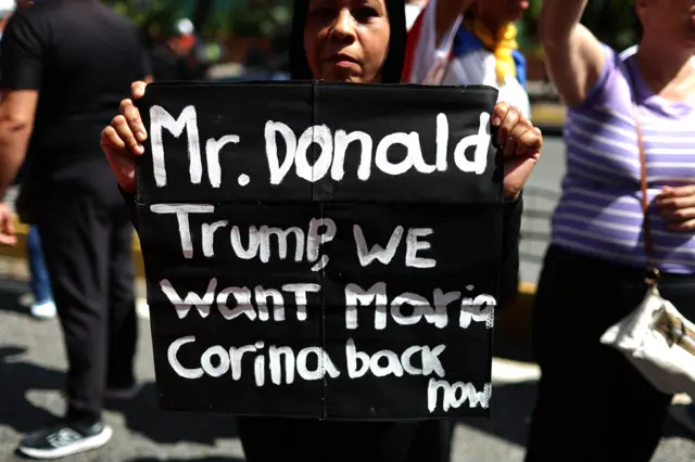 Una manifestante lleva un cartel con un mensaje en inglés en el que le pide a Donald Trump el regreso de María Corina Machado a Venezuela.