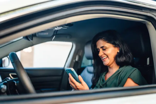 Mulher observa celular dentro de carro