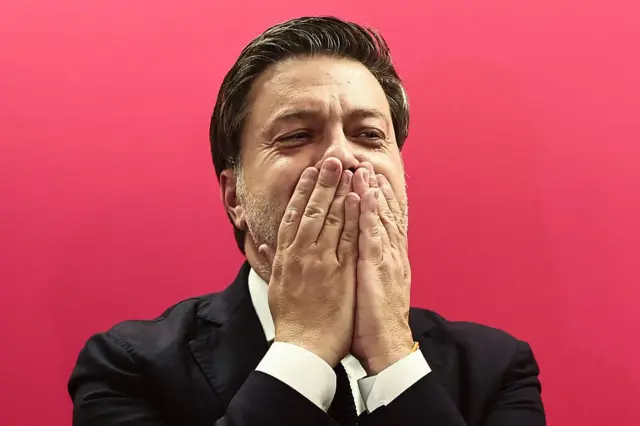 Бенуа Пайян на розовом фоне закрывает ладонями лицо