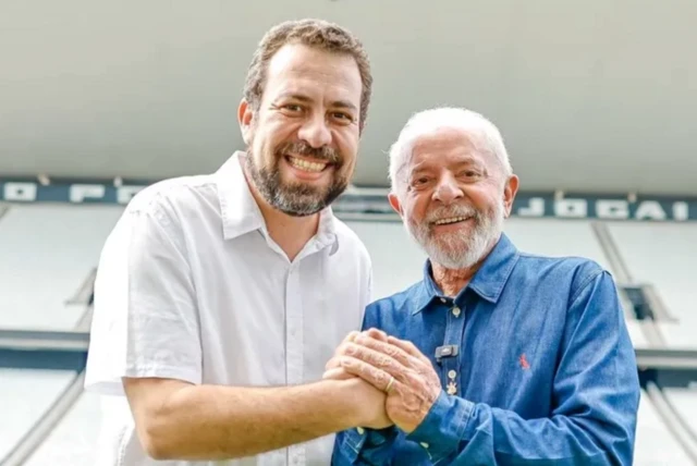 Lula e Guilherme Boulos de mãos dadas em um estádio de futebol