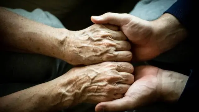 Manos de un adulto enfermo sostenidas por las manos de un pariente