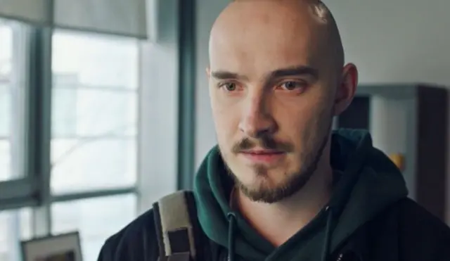 Лисий чоловік у зеленому худі дивиться вниз кадру 