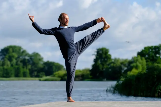 Un hombre hace una postura de yoga sobre uno de sus pies. 