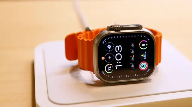 紐約大中央車站蘋果專賣店內展示的一隻 Apple Watch,它配有橘色錶帶,錶面顯示時間為1:03。(2023年12月)