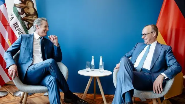 Фридрих Мерц и Гэвин Ньюсом сидят, улыбаясь друг другу, в креслах, оба в голубых костюмах и на голубом фоне