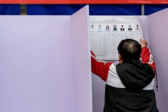 Một người đàn ông đang dán thông tin bầu cử tại một điểm bỏ phiếu cho cuộc bầu cử Quốc hội và Hội đồng nhân dân địa phương tại Hà Nội hôm 13/3/2026