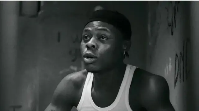 Aworan Mohbad. O wọ aṣọ awọtẹlẹ funfun, o si de fila dudu.