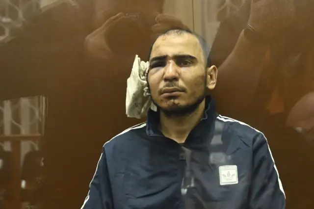 Saidakram Rajabalizoda with a large bandage on one ear, with his eye swollen and bruised