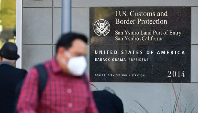 Un hombre con mascarillas, al que se ve borroso, frente a una placa que indica la el Puerto de Entrada Terrestre de San Ysidro en San Ysidro, California, el 7 de noviembre de 2021.  (Foto de FREDERIC J. BROWN/AFP via Getty Images)