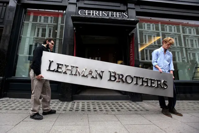 Duas pessoas seguram uma placa em apoio ao Lehman Brothers em frente à Christie's