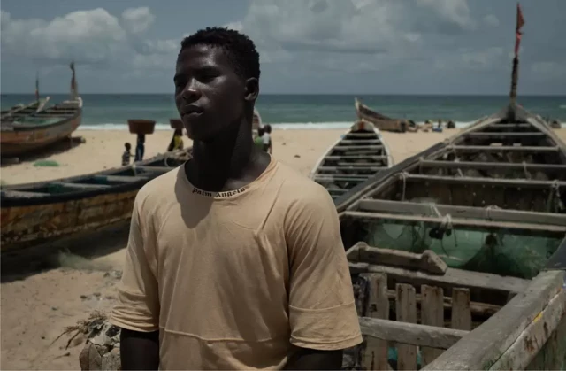 Assane Niang, pêcheur de 23 ans, sur la plage à côté d’une pirogue de pêche traditionnelle.
