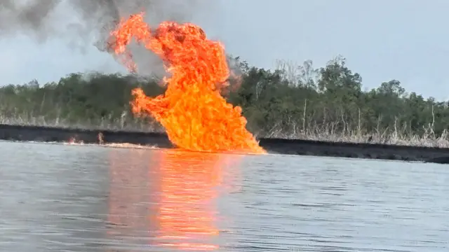 Flaming fire wey dey burn on top river wit mangrove for di background