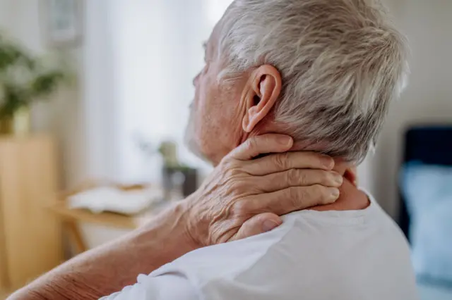 Un hombre mayor se toca el cuello, en un gesto de agotamiento y agobio.