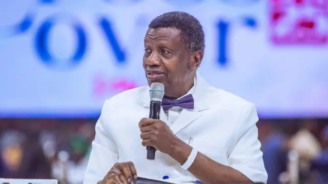 Pastor Enoch Adeboye wear all-white wit microphone for hand during di 2024 cross-over service.
