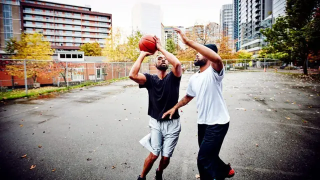 Irmãos disputando uma bola de basquete enquanto jogam em uma quadra de rua