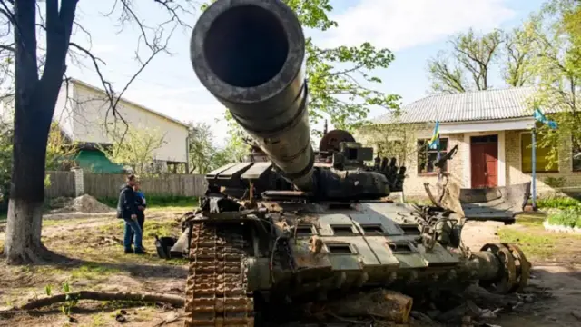 Warga lokal berdiri di sebelah tank Rusia yang hancur di Sloboda, Chernihiv, Ukraina - 8 Mei 2022.