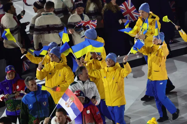 Sportisti i sportistkinje iz Srbije i Ukrajine mašu zastavama, u odelima u bojama nacionalnih zastava