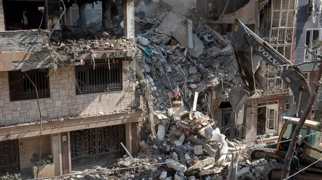 یک بیل مکانیکی در حال برداشتن آوار از یک ساختمان مسکونی است که در حمله امروز اسرائیل به تهران ویران شده است، ۱۳ ژوئن ۲۰۲۵ در تهران، ایران. صبح زود سیزدهم ژوئن، ایران مورد حمله هوایی اسرائیل قرار گرفت که سایت‌های نظامی و هسته‌ای و همچنین مقامات ارشد نظامی را هدف قرار داد.