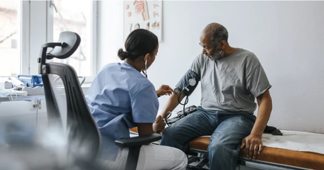رجل يجلس في مركز طبي وتجلس أمامه ممرضة تقيس له ضغط الدم.