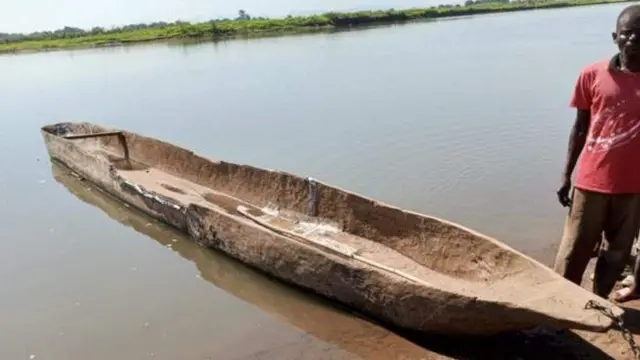 Ubwato bwo mu giti buri ku nkombe y'umugezi, iruhande rwabwo hahagaze umugabo