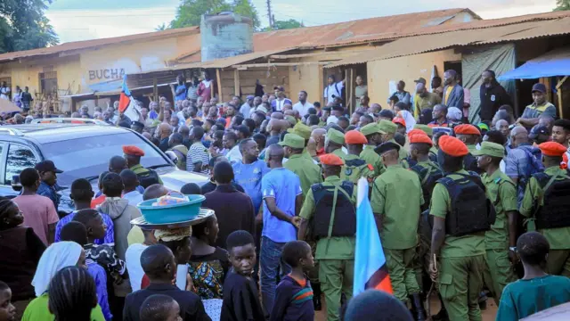 Imodoka ikikijwe n'imbaga y'abantu barimo n'abashinzwe umutekano bambaye imyenda ibaranga y'akazi. Ifoto yo ku itariki ya 9 Mata (4) mu mwaka wa 2025. 