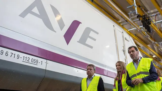 El ministro de Transportes, Óscar Puente, con una chaqueta amarilla pasa por delante de un AVE. 