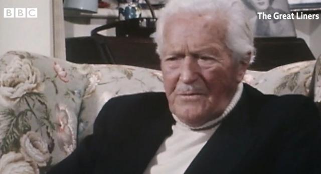 Frank Prentice, um homem branco idoso, de cabelos brancos de bigodes, sentado em um sofá com um olhar distante