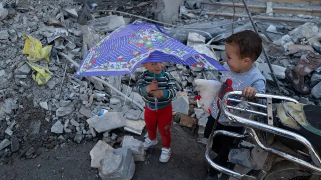 Devojčica se osmehuje bratu dok se igraju među ruševinama zgrade oštećene izraelskim napadom, usred privremenog prekida vatre između Libana i Izraela u Hušu blizu grada Tira