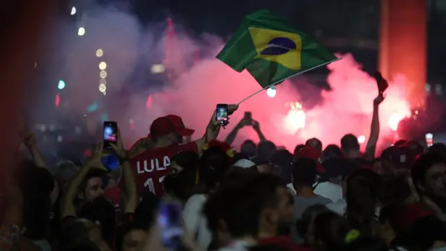 Bandeira do Brasil e dezenas de apoiadores de vermelho comemoram à noite