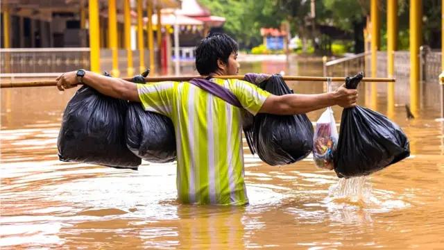 A man walks along a submerged road in Thailand after heavy rainfall caused flooding