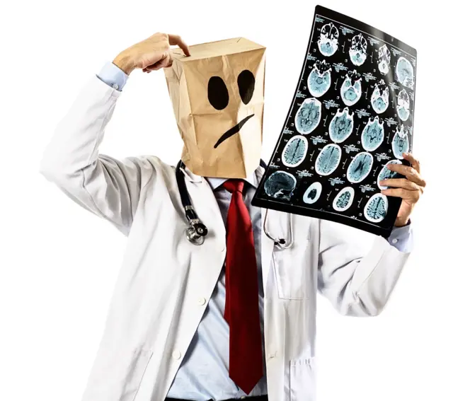 แพทย์สวมถุงกระดาษปิดหน้า มองภาพสมอง และเกาศีรษะ