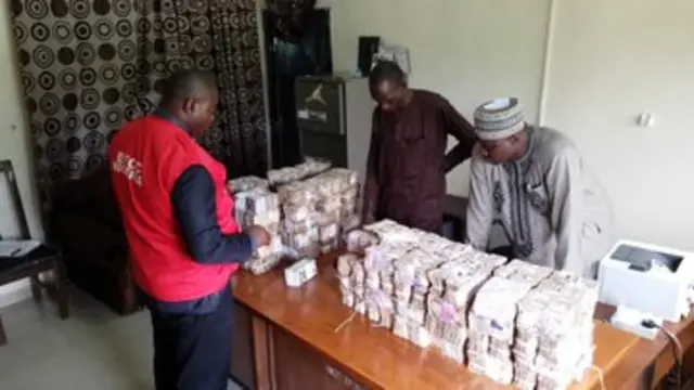EFCC officials tanda beside table wey money dey ontop