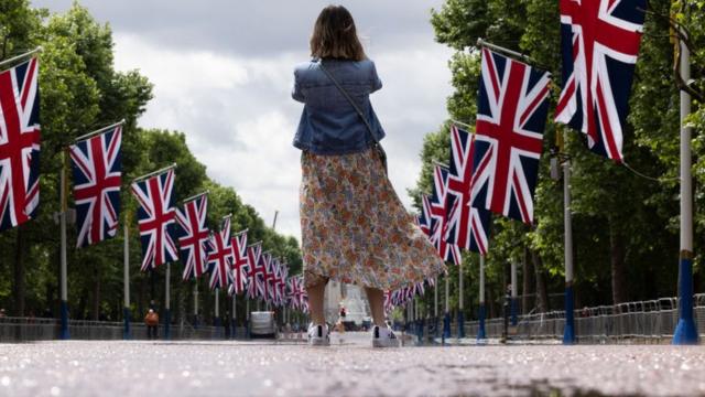 A woman takes a photo of Union flags lining the Mall in London in May 2022