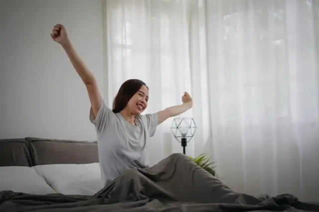 A woman stretches in bed in her own room.