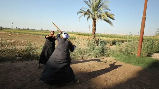 رجلان في حقل يرقصان رقصة التحطيب