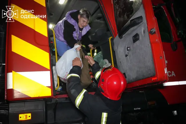 Рятувальник передає речі жінці, що схилилася до нього з авто ДСНС