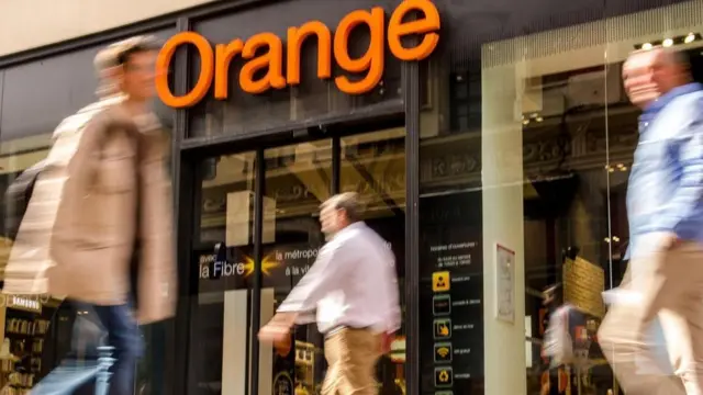 Personas caminando frente a una tienda de Orange