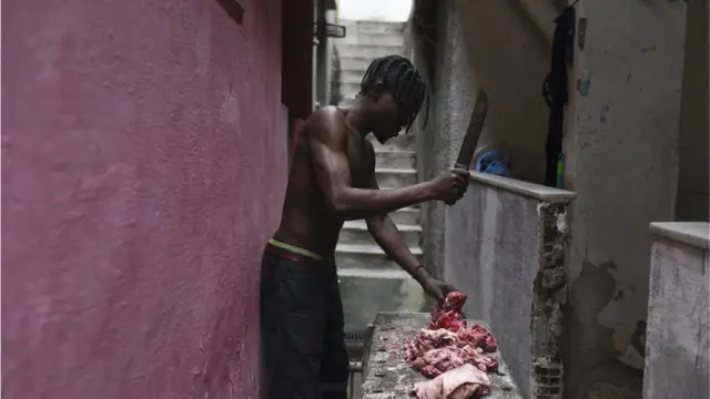 Wani mutum da babu riga a jikinsa, rike da kakkaifar wuka ya na datsa kashi da na nama a kusa da matakalar bene.