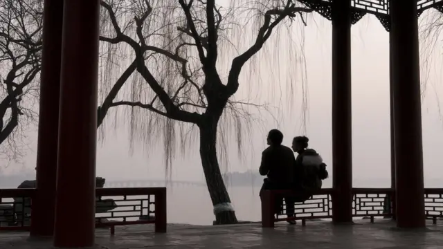 一对男女坐在北京颐和园的一个亭子里，远处是雾霾中 的十七孔桥