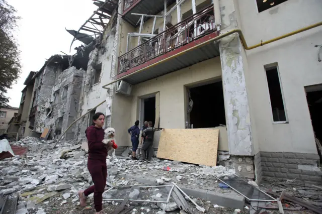 امرأة تحمل كلباً أمام مبنى سكني دمر جزئياً جراء القصف الروسي، خاركيف، شمال شرق أوكرانيا