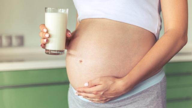 Una mujer embarazada sostiene un vaso de leche.