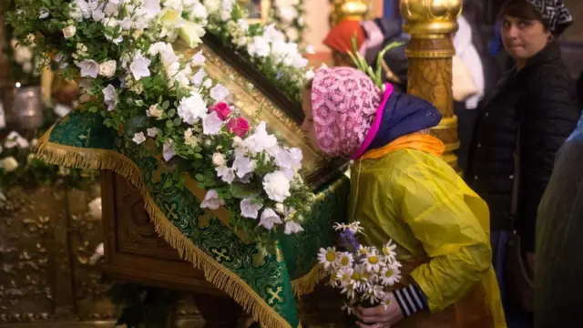 Mujer besando una figura en una iglesia ortodoxa.