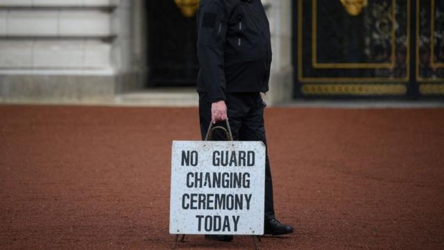 Um policial carrega uma placa dizendo 'não há troca de guarda hoje' do lado de fora do Palácio de Buckingham, em Londres