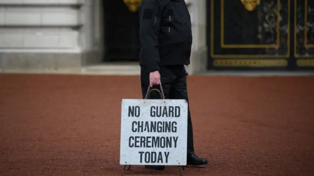 Um policial carrega uma placa dizendo 'não há troca de guarda hoje' do lado de fora do Palácio de Buckingham, em Londres