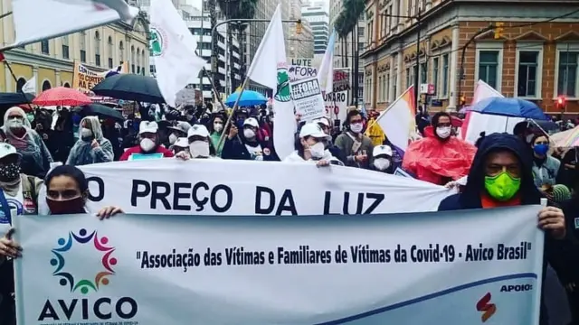 Paola e Gustavo seguram cartaz enquanto outras diversas pessoas protestam e carregam mensagens contra o governo federal