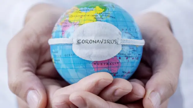 Pequeno globo representando a Terra, com máscara estampando a palavra 'coronavírus'