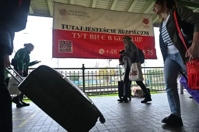 Жінки з валізами йдуть повз напис на пероні "Тут ви в безпеці"